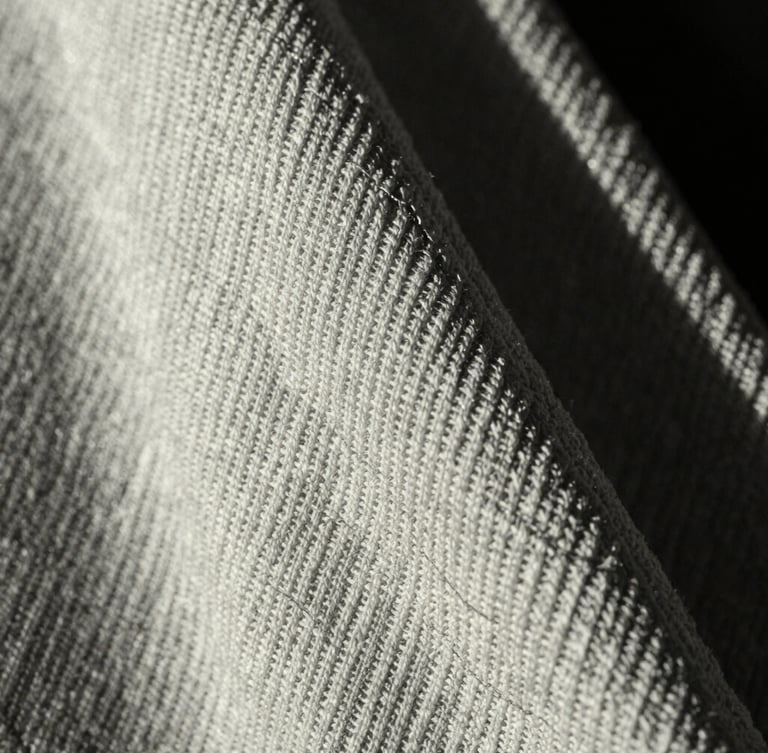 Macro close-up of heavy 400GSM loopback terry fabric texture, showing the dense knit structure and clean engineered stitching, high-contrast dramatic side-lighting, monochrome tones.