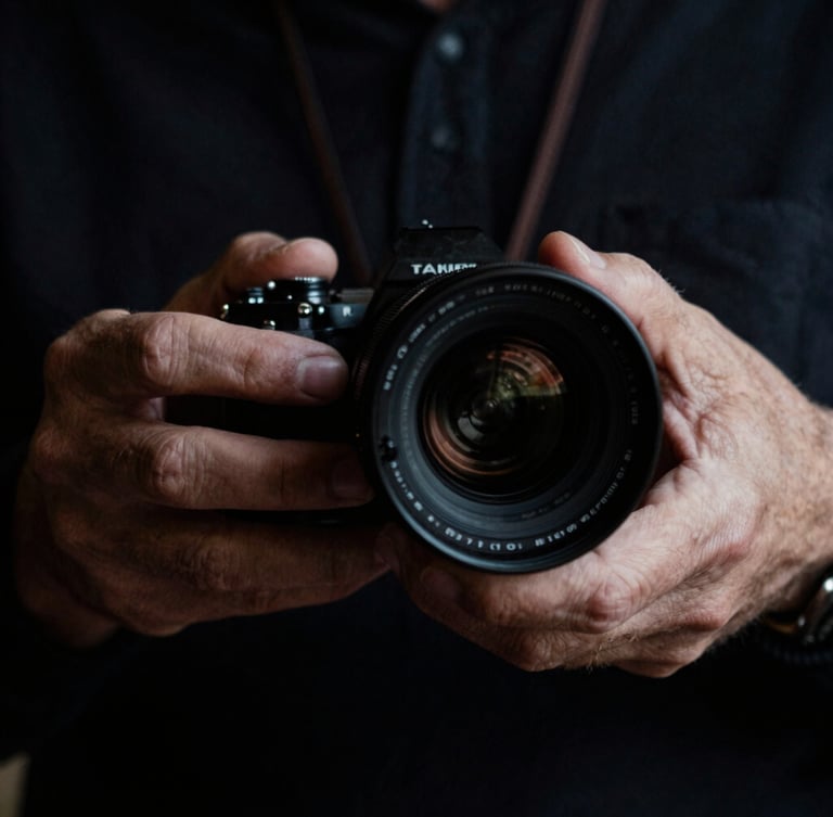 Moody close-up of a director's hands adjusting a vintage anamorphic lens, dramatic side lighting, deep shadows, rich dark tones, 35mm film look.