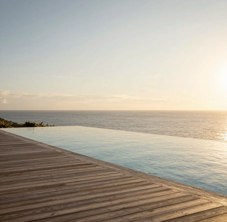 Extreme wide environmental shot of a private infinity pool merging with the open ocean at golden hour, minimalist wooden deck, warm low sunlight