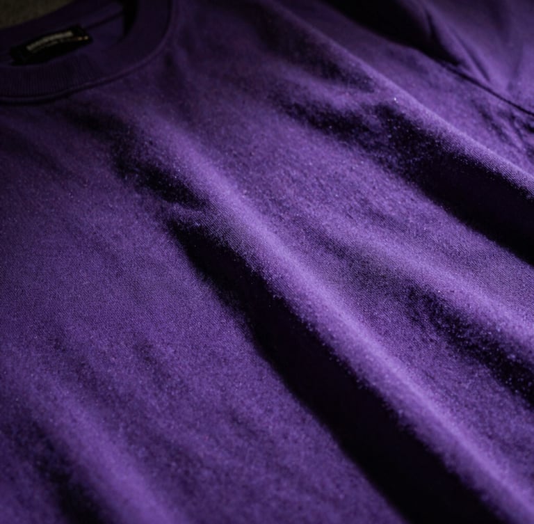Close-up of premium heavy-weight violet cotton fabric with high-contrast shadows, embroidered details visible under harsh overhead light