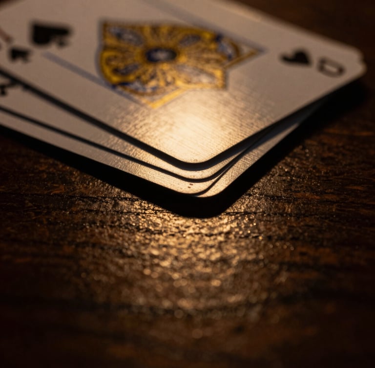 Close-up macro shot of elegant playing cards with gold-gilded edges, dramatic low-key lighting, deep shadows, warm gold light reflecting off a dark wooden surface.