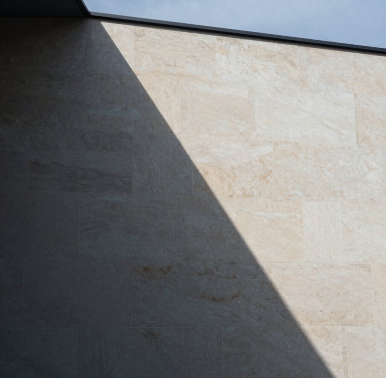 A close-up architectural crop of sharp geometric shadows falling across a warm alabaster limestone facade, cool overcast daylight, 35mm editorial photography.