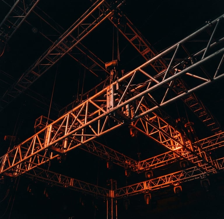 Close-up of a complex metal truss structure under dramatic stage lighting, deep shadows, vibrant orange light accents, architectural lines, wide-angle, sharp details, 35mm