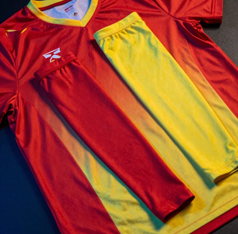 Overhead flat-lay of a matching tournament-grade jersey and compression arm sleeve set in vibrant crimson and canary yellow, high-contrast athletic studio lighting with dramatic blue rim lights reflecting off the technical fabric, sharp detail, 85mm lens