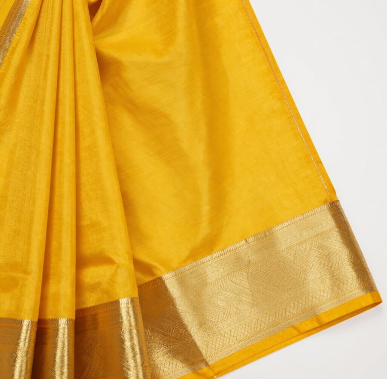 Close-up macro shot of vibrant marigold yellow silk saree fabric, showing intricate gold zari thread weaving and rich textile texture under soft daylight.