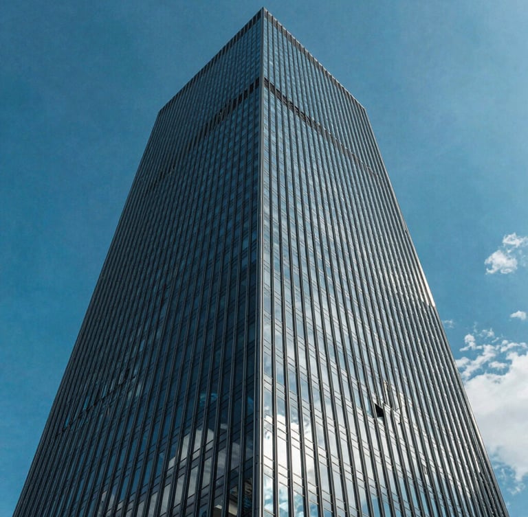 Low-angle architectural photograph of a modern glass skyscraper corner piercing a vibrant blue sky, crisp daylight, sharp reflections of clouds on glass.