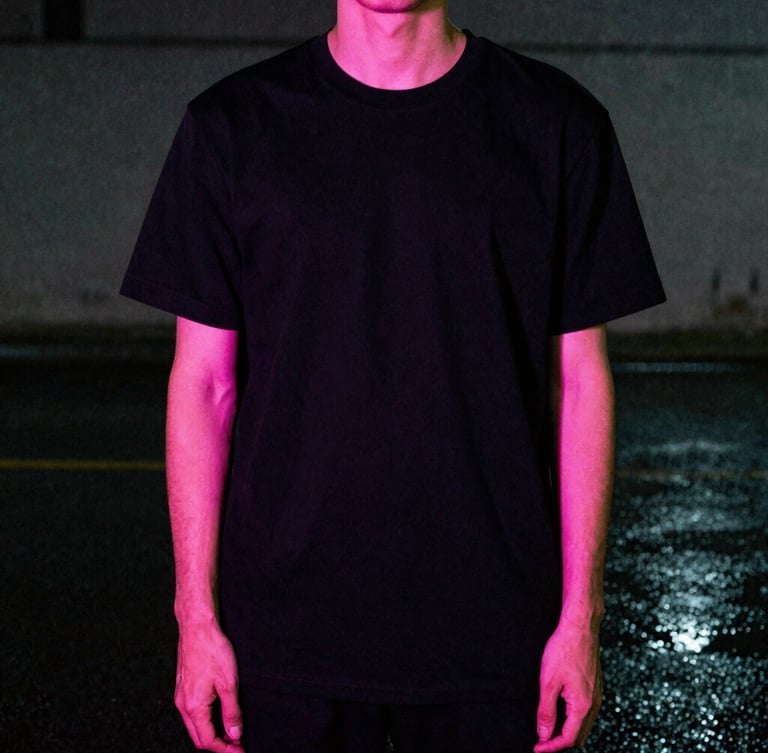 Low-angle cinematic shot of a model wearing a black graphic tee under neon pink rim lighting, wet pavement, dark concrete background, 35mm film grain