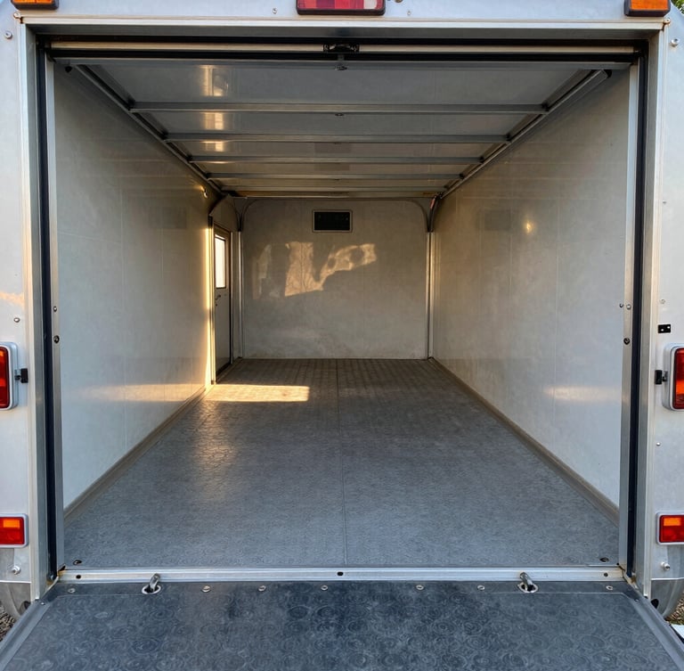 Wide-angle interior shot of the 14-foot garage cargo space in the Wolfpack trailer, clean grey coin flooring, heavy-duty steel tie-down rings flush in the deck, natural daylight pouring in from the open ramp door.