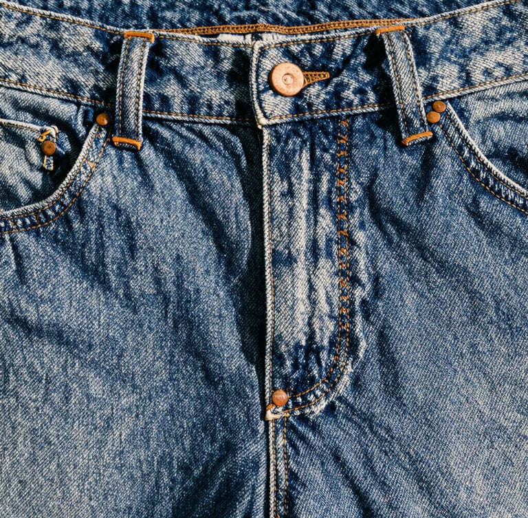 Close-up of heavy raw denim texture showing triple-stitched seams and copper rivets under harsh natural daylight, high contrast, 35mm film photography.