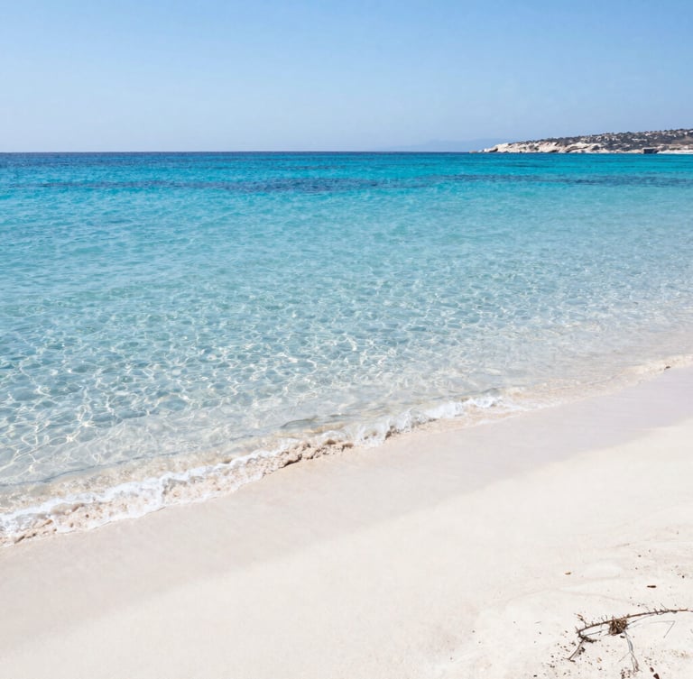 Wide environmental shot of a sun-drenched Greek beach with crystal-clear turquoise waters and white sand, midday sun reflecting on water, bright coastal photography