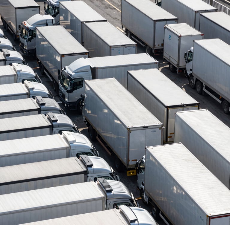 Clean geometric overhead shot of an organized fleet yard with aligned commercial transport trucks, overcast daylight, sharp metallic reflections