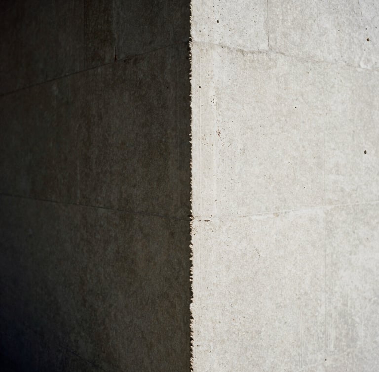 Grainy 35mm close-up of harsh sunlight hitting a raw concrete pillar, deep architectural shadow, minimalist high-contrast composition