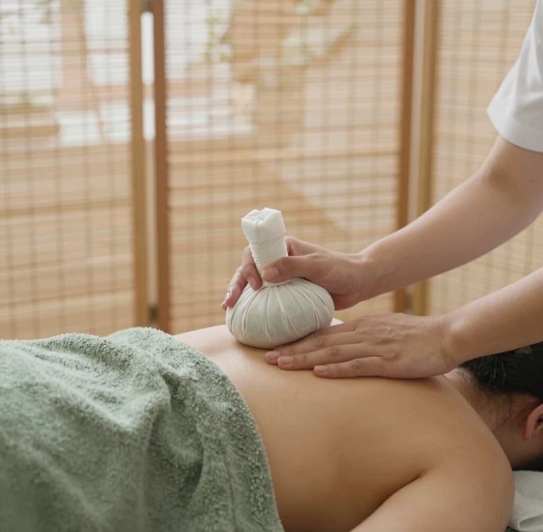 A professional therapist gently placing warm herbal compress on a shoulder, soft natural lighting filtering through bamboo screens, warm editorial photography, 35mm, muted moss green and warm stone tones