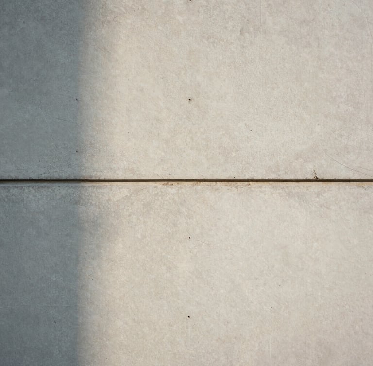 Straight-on architectural elevation of a concrete and honed travertine wall joint, soft natural daylight casting subtle shadows, minimal spatial composition.