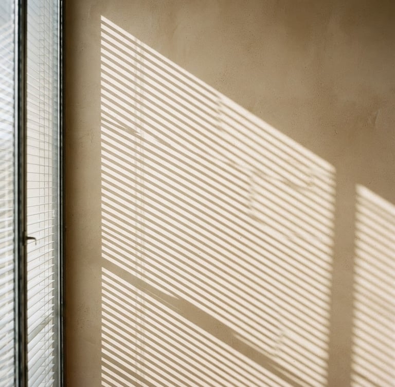 Minimalist architectural photography of elegant blinds casting geometric shadows on a warm plaster wall, bright natural daylight, neutral warm tones, 35mm