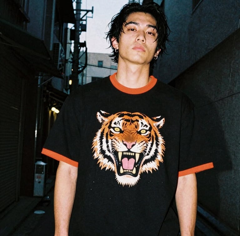Low-angle heroic shot of a streetwear model in a dark Tokyo alley at dusk, wearing a heavy-weight black tiger-graphic t-shirt, neon orange rim light, high contrast, 35mm film.