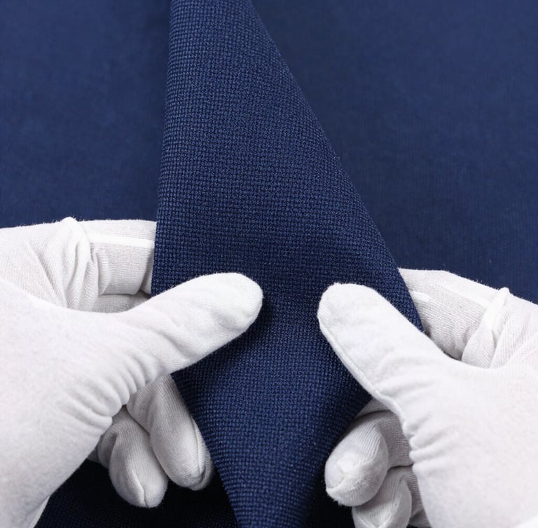 Macro close-up shot of hands in white gloves inspecting a roll of tightly woven navy fabric, showing texture and thread count, under bright studio lighting, clean and precise.