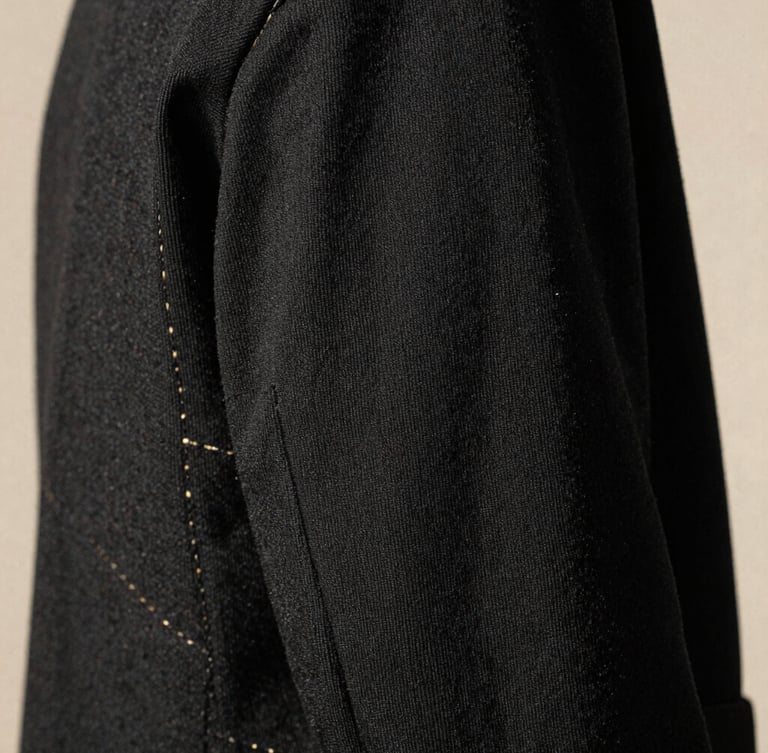 Macro close-up of heavy-weight black cotton fabric texture, golden sunlight highlighting the precise stitching, minimalist studio setting, 35mm film grain