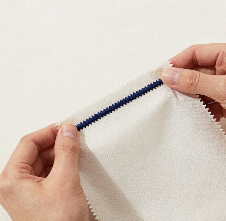 Crisp studio product photography of hands holding a physical fabric swatch with precise navy embroidery, bright neutral lighting, detailed fabric textures, sharp focus