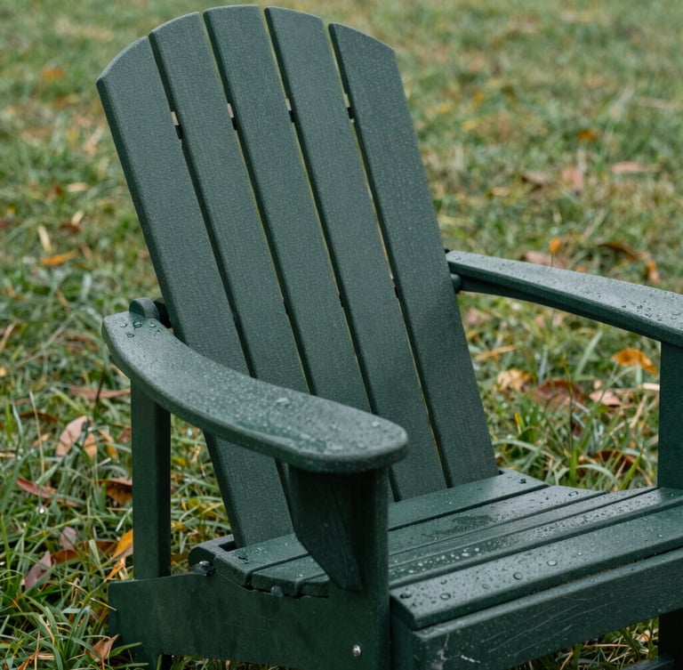 Close-up of a dark forest green Adirondack chair on a dew-covered lawn, overcast natural daylight, showing thick material texture and rugged construction