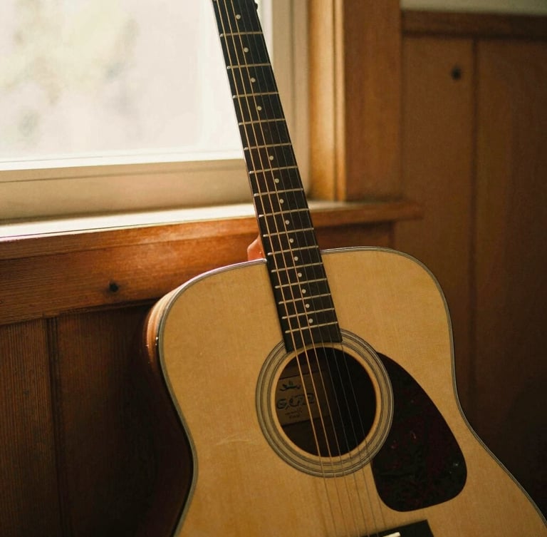 Intimate medium shot of an acoustic guitar leaning against a wooden wall, soft golden light filtering through a window, warm sepia tones, 35mm film style