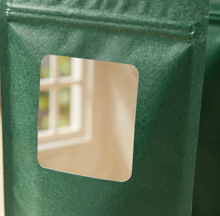 Macro close-up of folded forest green packaging prototypes showing clean custom die-cuts, natural side-lit window daylight, high texture detail.