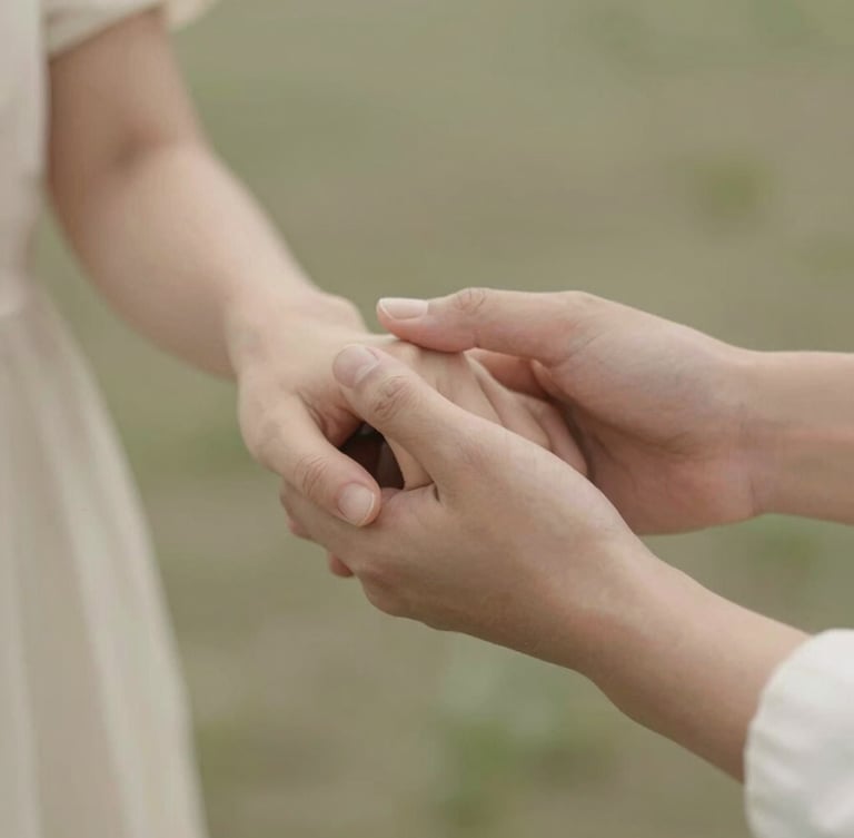 Warm editorial photography of soft diffused daylight falling on two hands gently holding each other, warm cream and sage tones, gentle focus, shallow depth of field, peaceful sanctuary atmosphere.