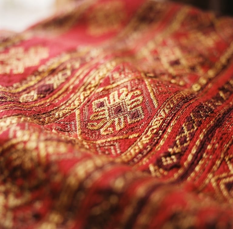 Close-up of intricate hand-woven Bhutanese textile with rich crimson and gold threads, warm natural window light, shallow depth of field, 35mm
