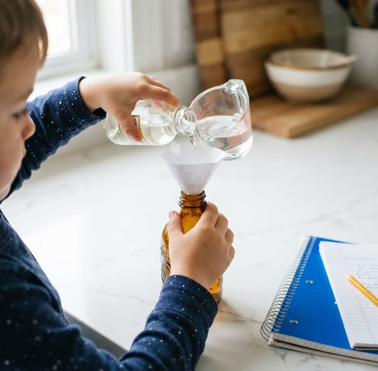 Close-up of a child's hands carefully pouring vinegar into a glass bottle using a small paper funnel, bright natural daylight, clean white kitchen counter background, energetic blue accent on a notebook nearby, sharp focus, 35mm