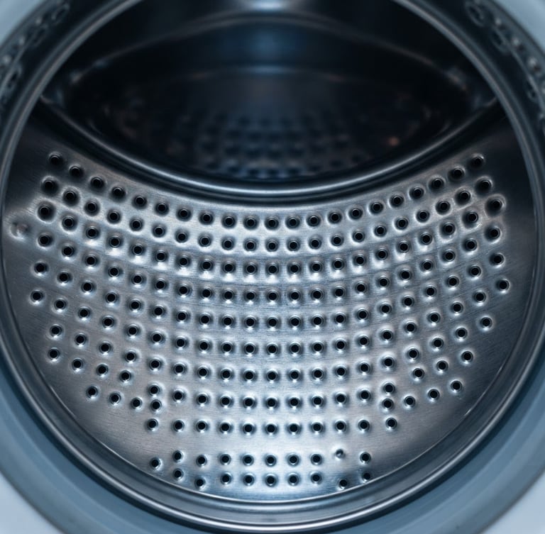 Straight-on macro shot of a clean stainless steel washing machine drum interior, bright workshop lighting, sharp focus on metallic texture, 50mm