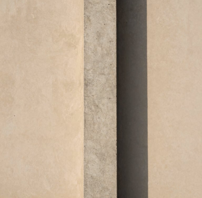A raw concrete column casting a soft, long shadow on a warm-toned plaster wall, minimalist architectural photography, diffused natural daylight
