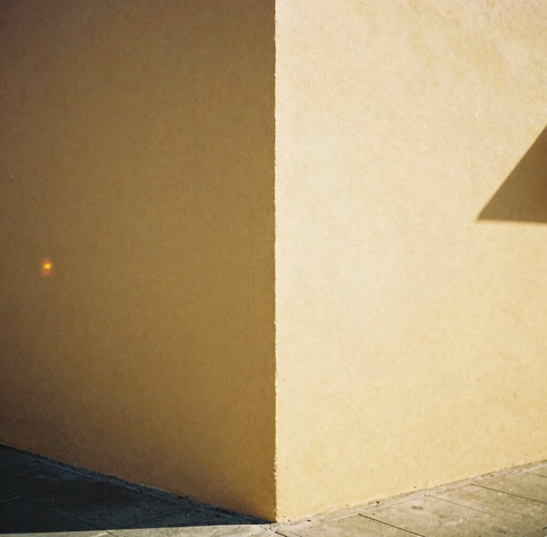 A raw, unedited 35mm film photograph of a sun-drenched street corner, warm analog film photography with visible light leaks and soft focus, saturated golden tones