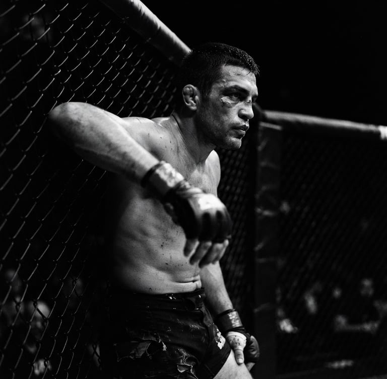 Dramatic high-contrast black and white portrait of a focused MMA fighter leaning against a chain-link cage, harsh directional key light, deep shadows, 35mm lens