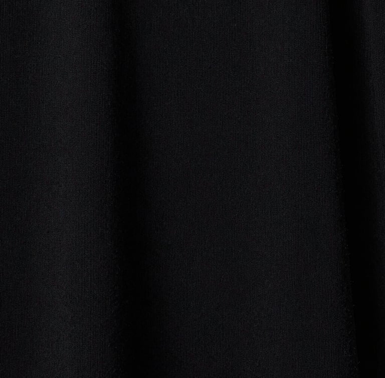 Extreme close-up on the heavy, custom-milled loopback cotton texture of a black garment, high-contrast studio lighting, showing the raw weave detail.