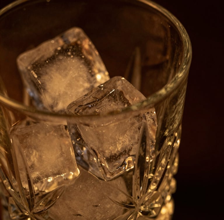 Close-up macro of a crystal mixing glass, clear ice block reflecting low-key warm amber light, dark moody background, shallow depth of field, 35mm