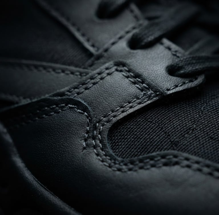 Extreme close-up of a luxury sneaker stitching, dramatic studio rim lighting, deep black and charcoal tones, sharp focus, 85mm lens