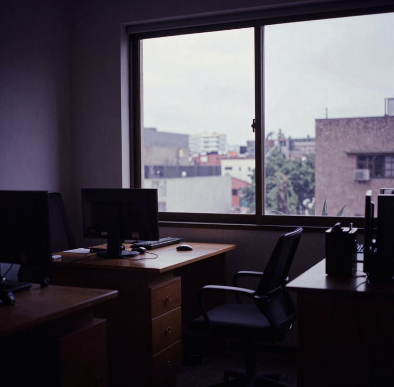 Moody film photography of a CDMX production office interior, soft overcast daylight through a high window, deep shadows, cinematic 35mm