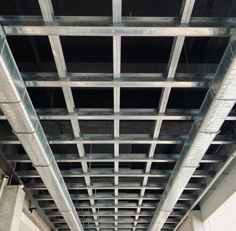 High-contrast architectural view looking directly up at a perfectly aligned ceiling grid of exposed stainless steel ductwork and conduit runs, cool ambient daylight.