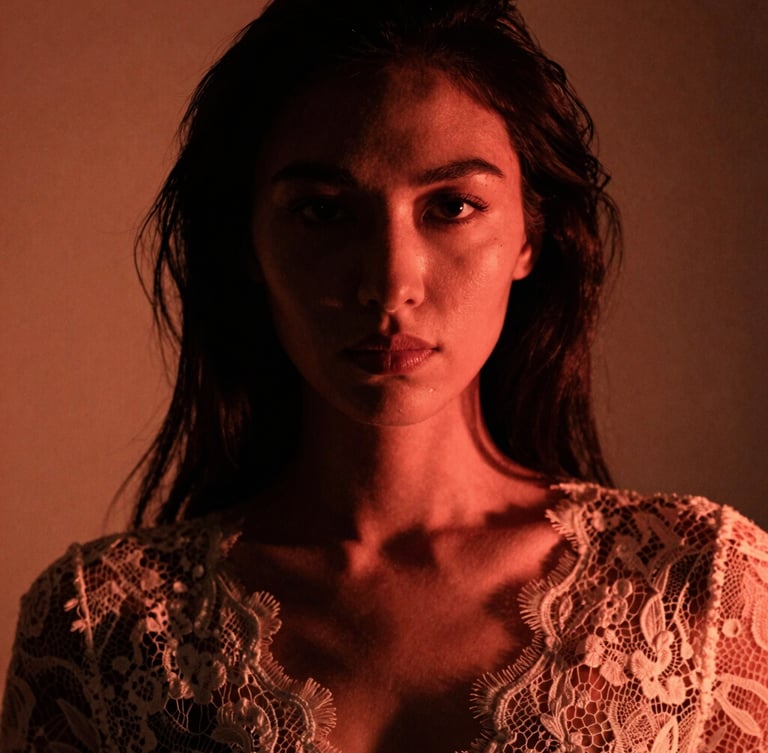 Close-up artistic portrait of a woman in elegant lace, dramatic low-key lighting with deep shadows and soft warm neon backlighting, high-contrast, fine 35mm film grain, editorial style.
