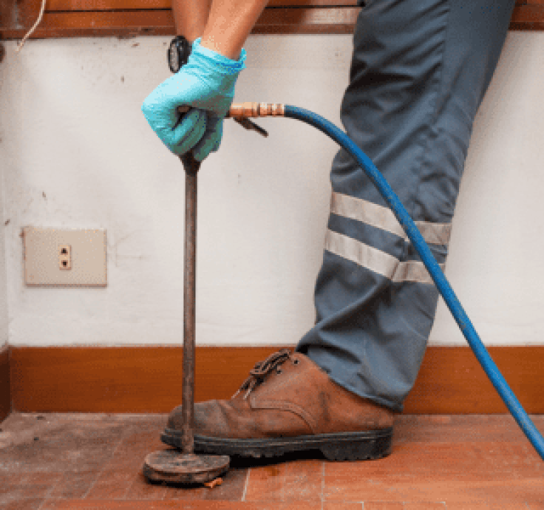 Professional pest control technician using a soil injector for termite treatment in a home.