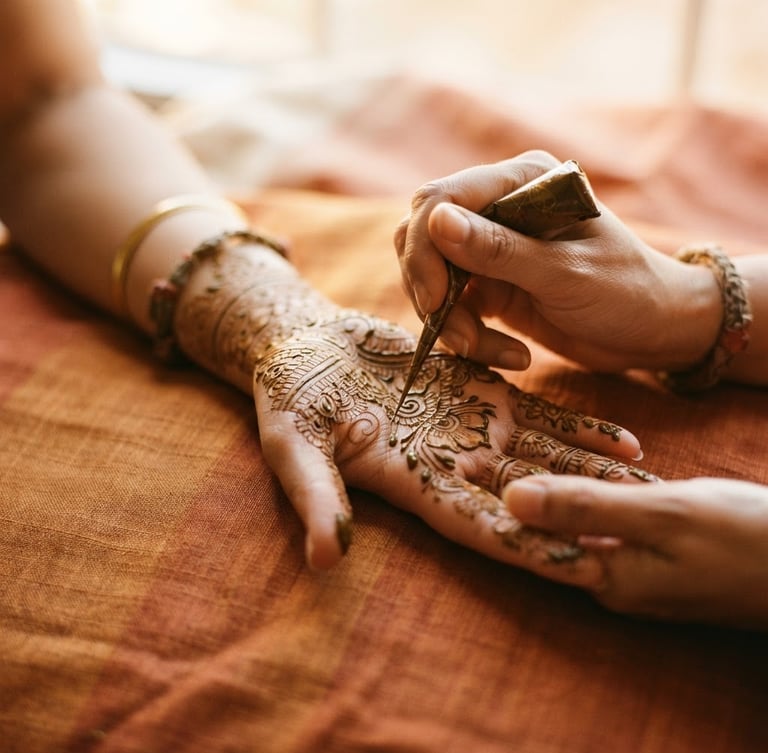 Close-up of hands resting on raw silk, artist applying intricate mehendi lines with a natural henna cone, warm diffused window light, shallow depth of field, 35mm