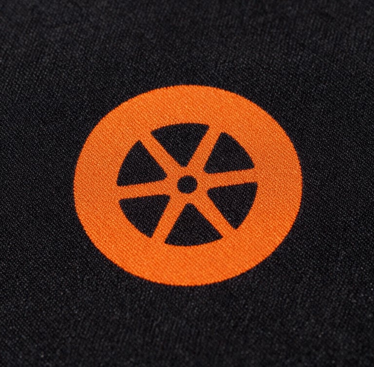 Extreme close-up of raised safety orange print texture on heavy-weight black cotton fabric, direct high-contrast sunlight emphasizing the weave.