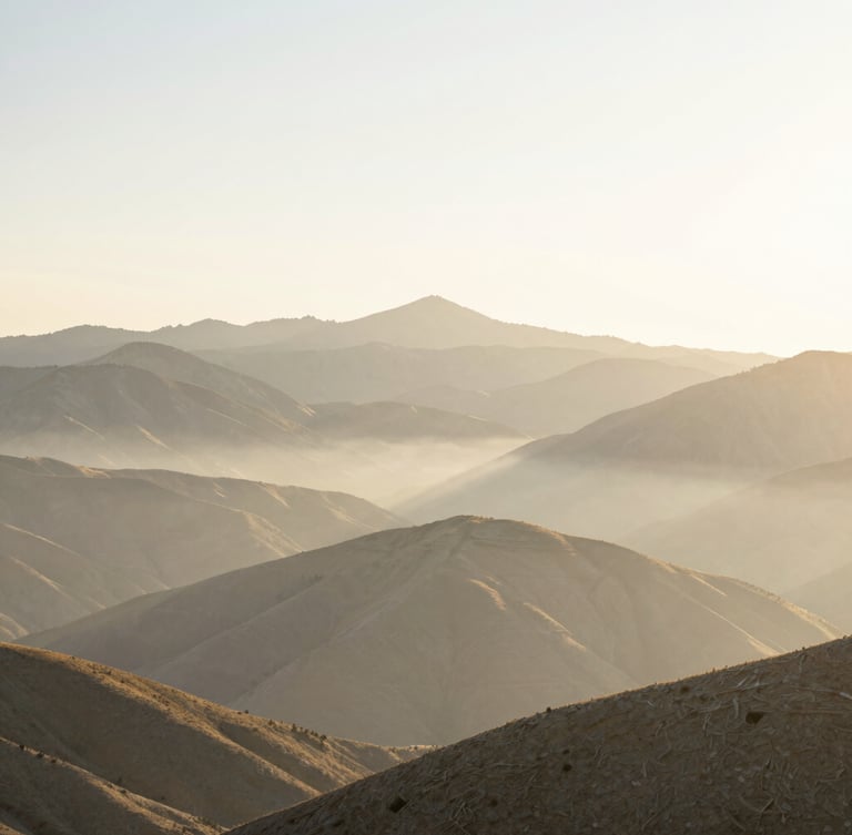 Expansive natural Utah mountain landscape at dawn, first morning light hitting the peaks, soft golden mist, wide environmental shot with generous negative space, airy high-key lighting