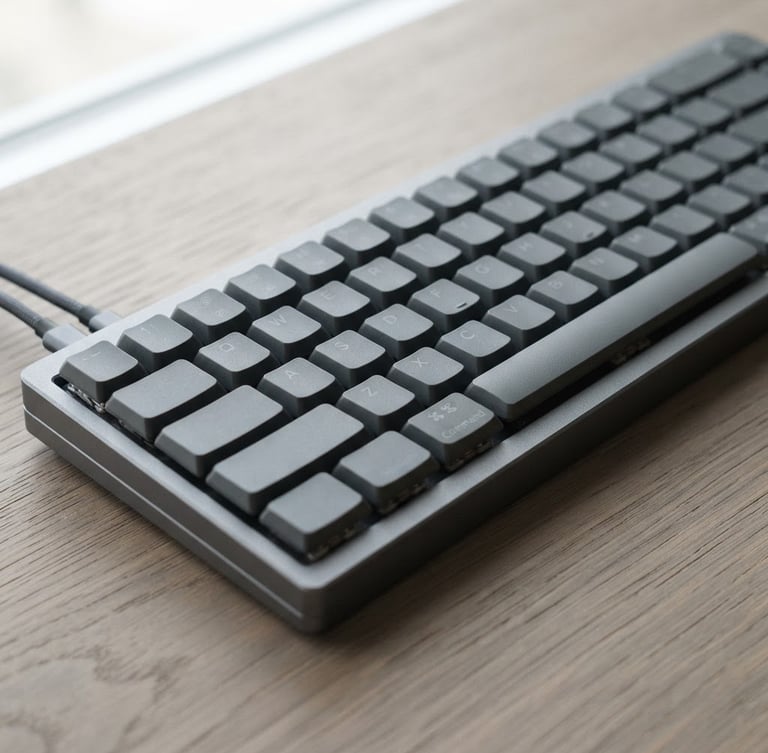 Close-up of a sleek physical aluminum keyboard on a warm gray wooden desk, soft diffused natural light, minimalist editorial photography, 35mm lens