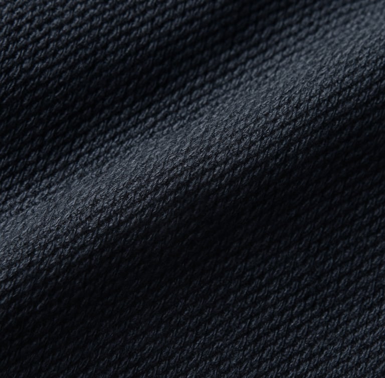 Macro close-up of deep navy heavy-weight cotton fabric, emphasizing the tight weave and texture, soft studio side-lighting, rich cream and deep navy tones.