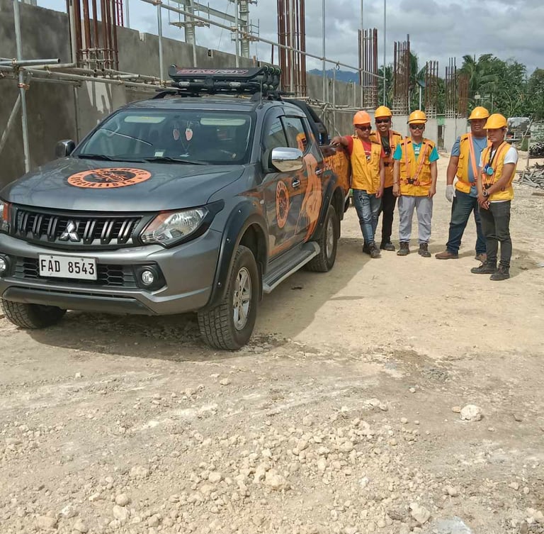 Construction workers in safety gear stand by a Mitsubishi pickup truck at a building site.