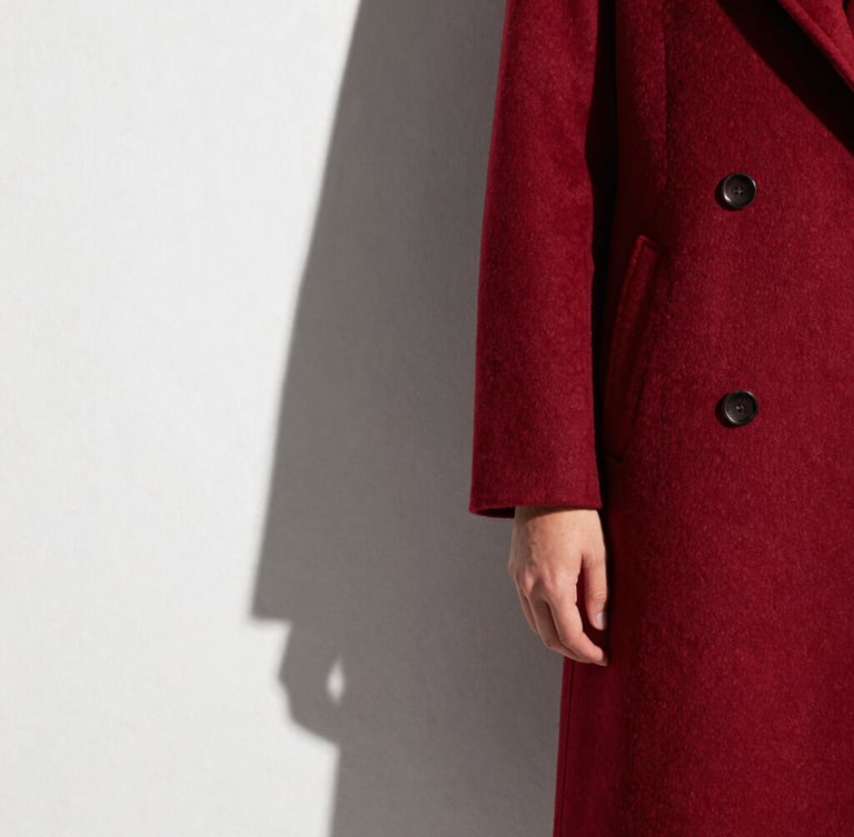 Architectural shadows cast on a structured deep crimson wool coat sleeve, high-contrast natural light, crisp parchment background, editorial fashion crop
