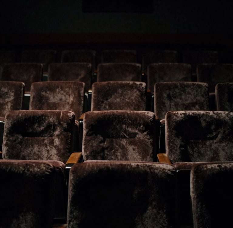 Dramatic low-key cinematic shot of a dark theater interior, faint light catching the edges of empty velvet seats, 35mm anamorphic lens style.