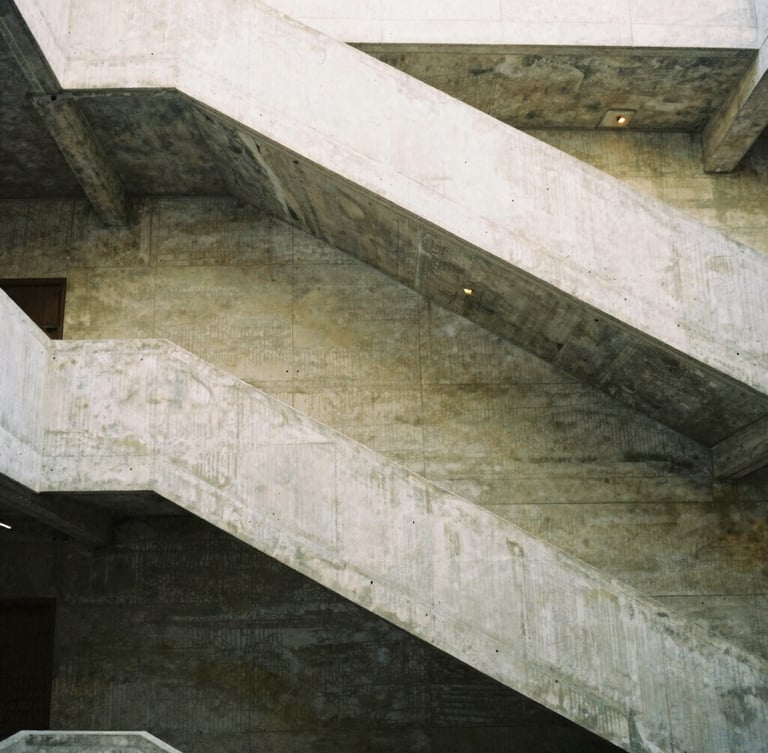 A tall vertical portrait of a concrete staircase winding upward, sharp architectural lines, soft diffused daylight falling from above, medium-format film style.