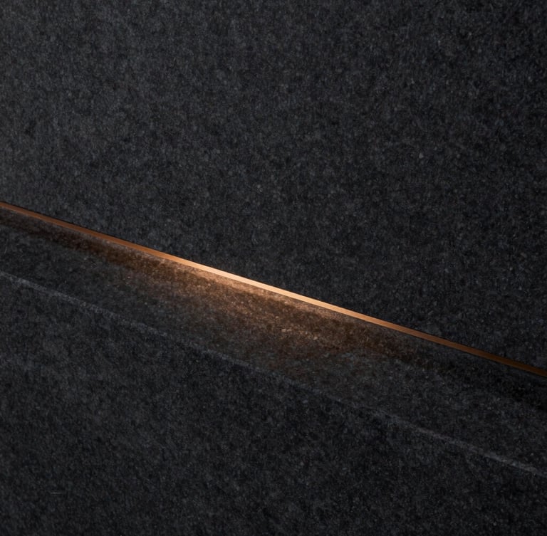 Macro shot of dark charcoal stone with a single warm bronze linear light reflection, minimalist architectural detail, 35mm